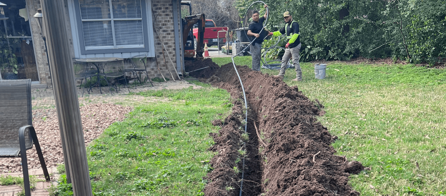 Electricians installing underground electrical wiring with trenching equipment outside a home in Montgomery county tx