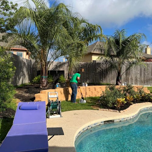 Man landscaping backyard pool area.