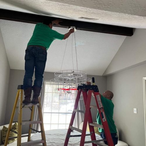 Two men installing a chandelier.