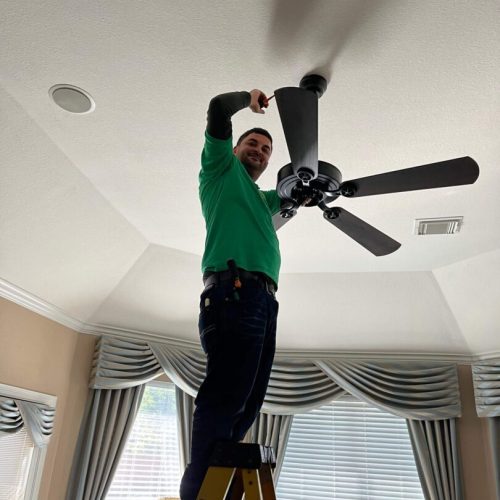 Technician installing ceiling fan on ladder.